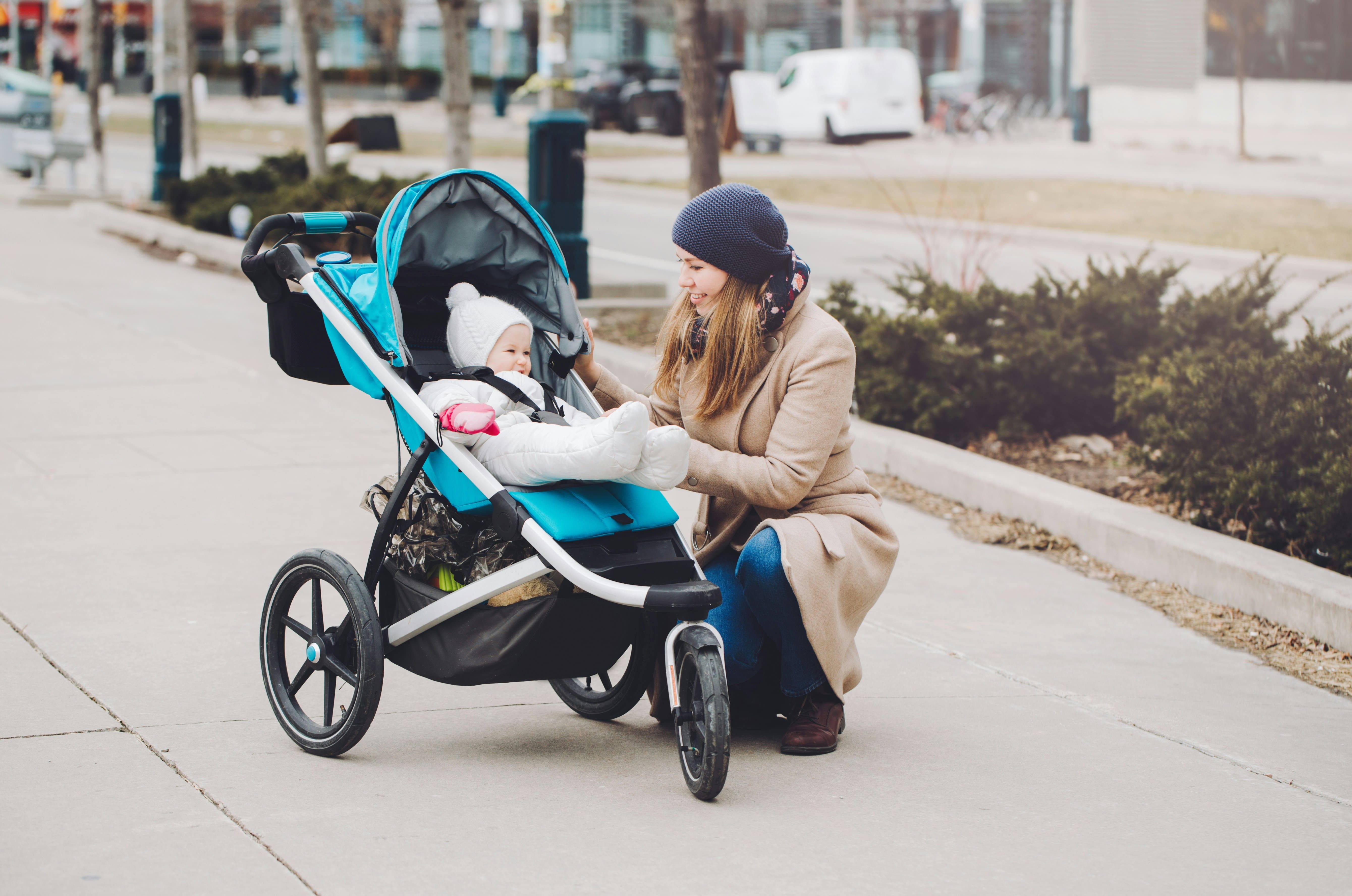 A mother smiling with her baby seated in a stroller outdoors